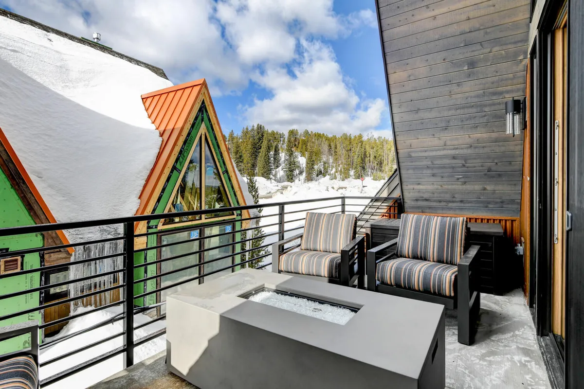 A tranquil exterior seating area features modern furniture, a fire pit, and a snow-covered landscape, with unique neighboring buildings visible in the background. The setting is ideal for stargazing, cozy evenings, or gathering with friends outdoors.