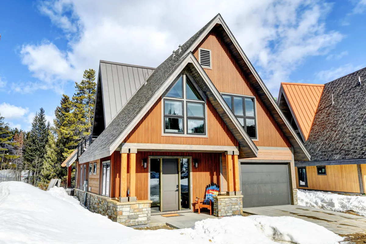 This exterior shot features the chalet's iconic A-frame structure with large windows and colorful chairs set out on the porch, inviting relaxation and gatherings in the beautiful natural surroundings.