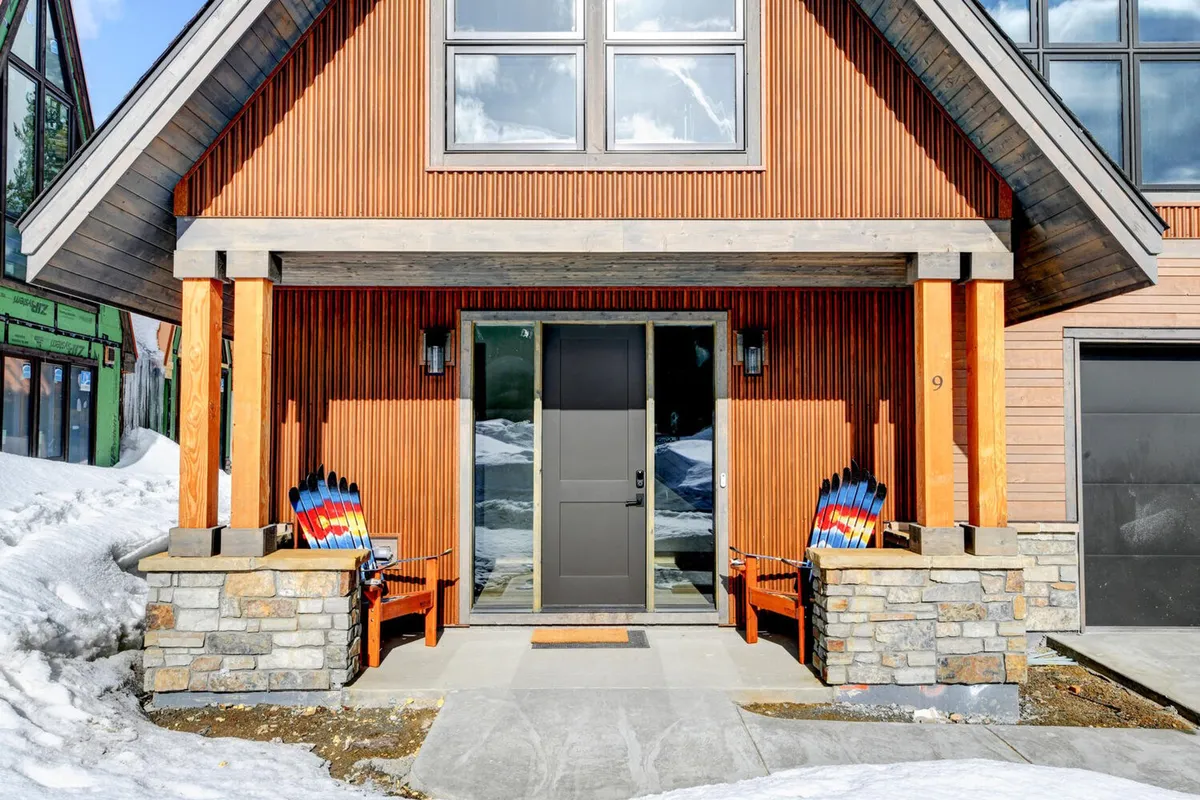 The inviting front porch features stone pillars, wooden benches, and colorful sleds, set against a snowy landscape. It invites residents and guests to relax outdoors, greet friends, or enjoy winter activities right at the doorstep.