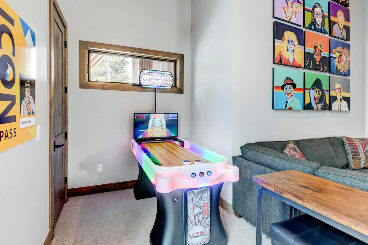 An interior rec room equipped with an air hockey table, vibrant artwork, a cozy sofa, and a wooden table, creating a lively space for friendly competition and socializing.