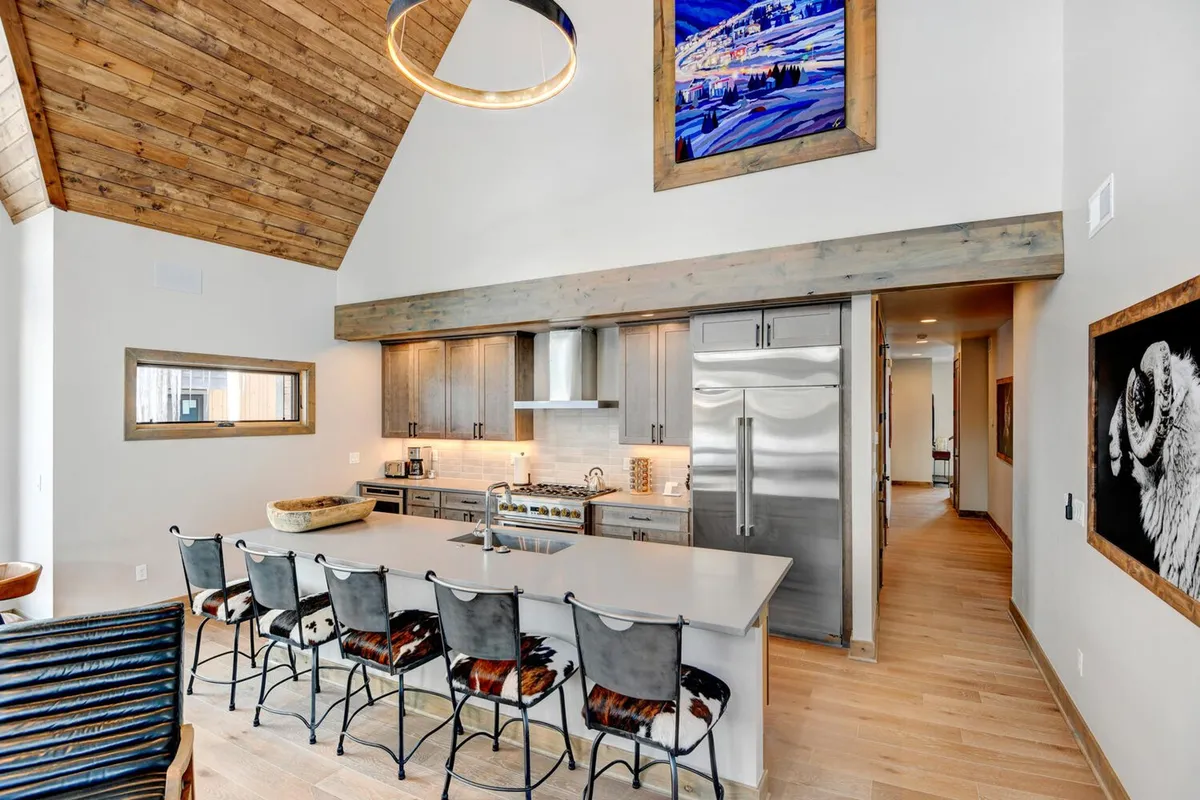 A modern kitchen highlighted by a large island with bar seating, wooden beams, stainless steel appliances, and inviting decor. The kitchen is arranged for both cooking and socializing, seamlessly connecting with the living areas.