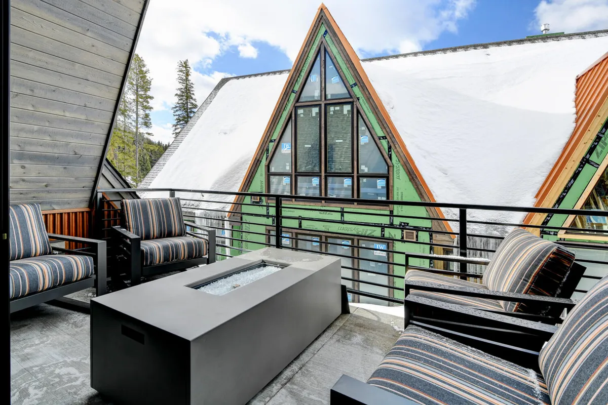 An upper deck furnished with modern chairs grouped around a sleek fire table, set beneath a contemporary architectural roof. The snow-covered roof and open-air setting create a cozy and contemporary vibe, perfect for relaxing and enjoying views regardless of the season.