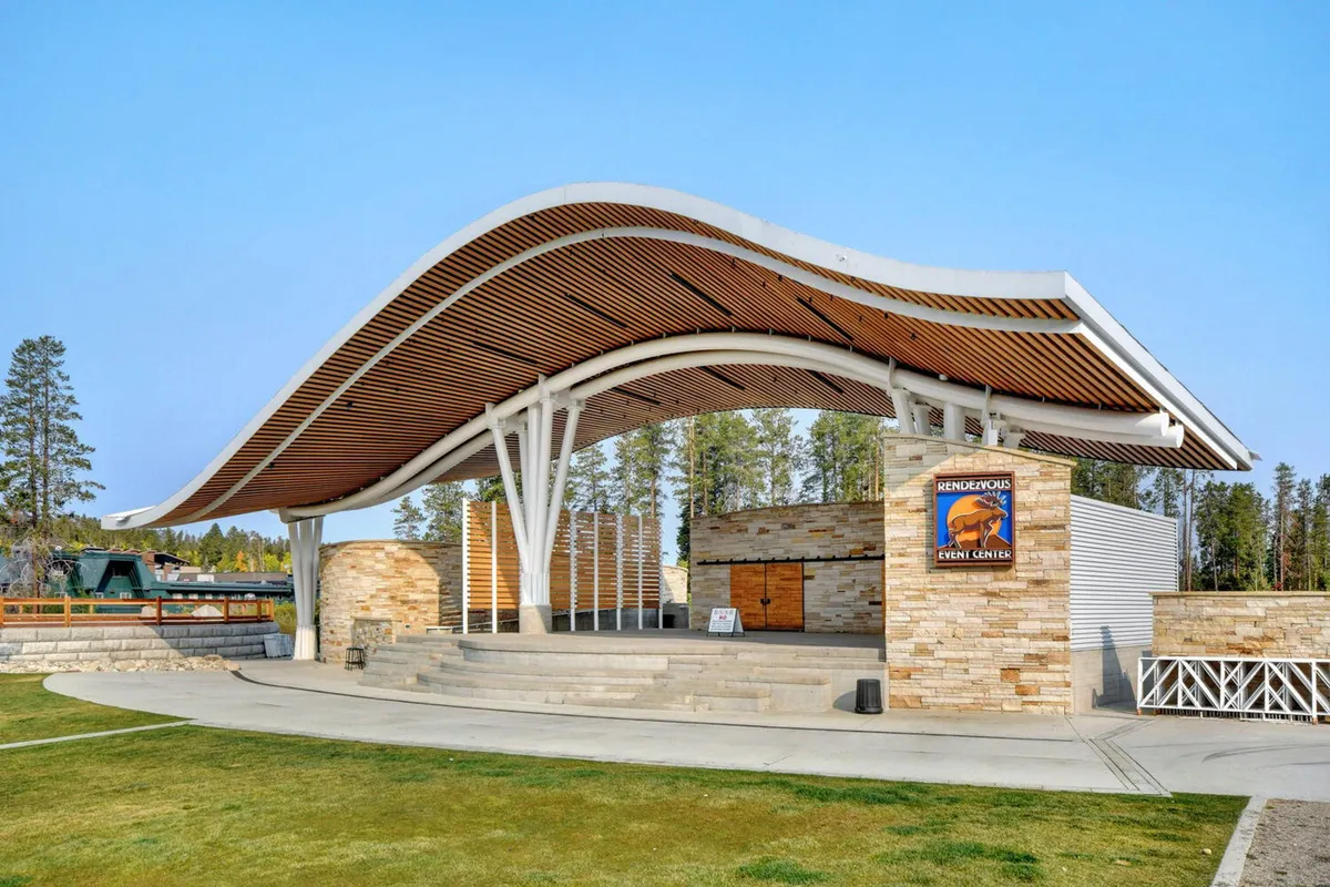 This image captures the Rendezvous Event Center at Hideaway Park, with its unique curved roof, stone architecture, and open stage area set up for community events and concerts. The scene exudes anticipation for live performances and festive gatherings.