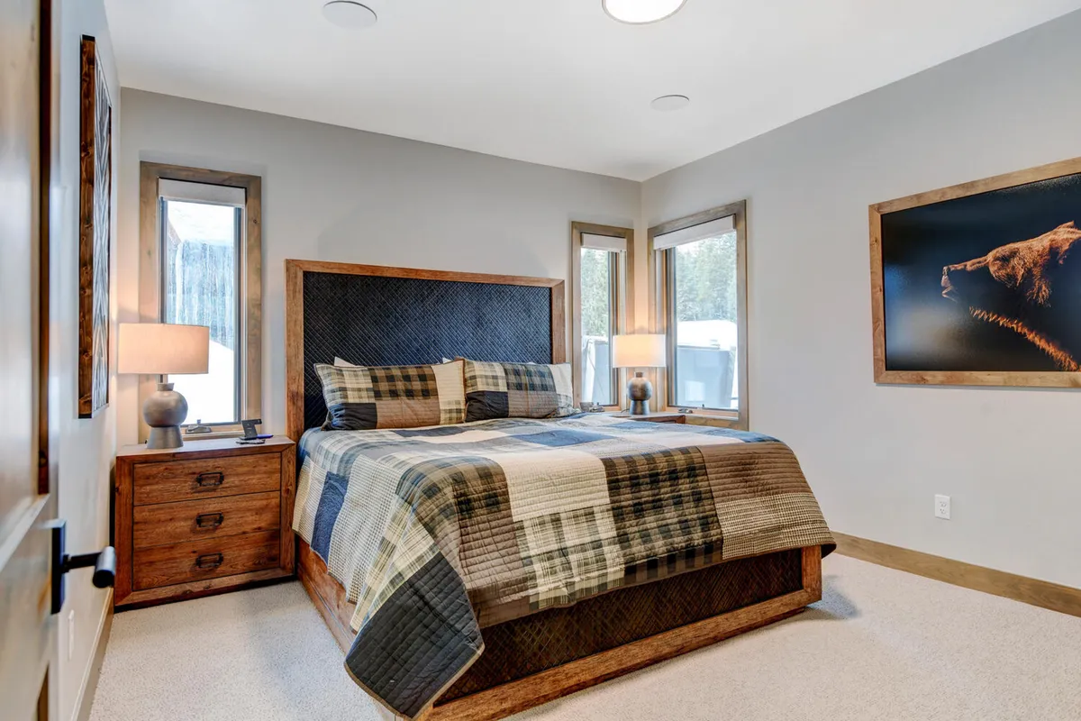 A bedroom featuring a bed with plaid bedding, rustic wooden headboard, and table lamps. The room feels warm and inviting, ideal for relaxing and enjoying quiet moments in the mountains.