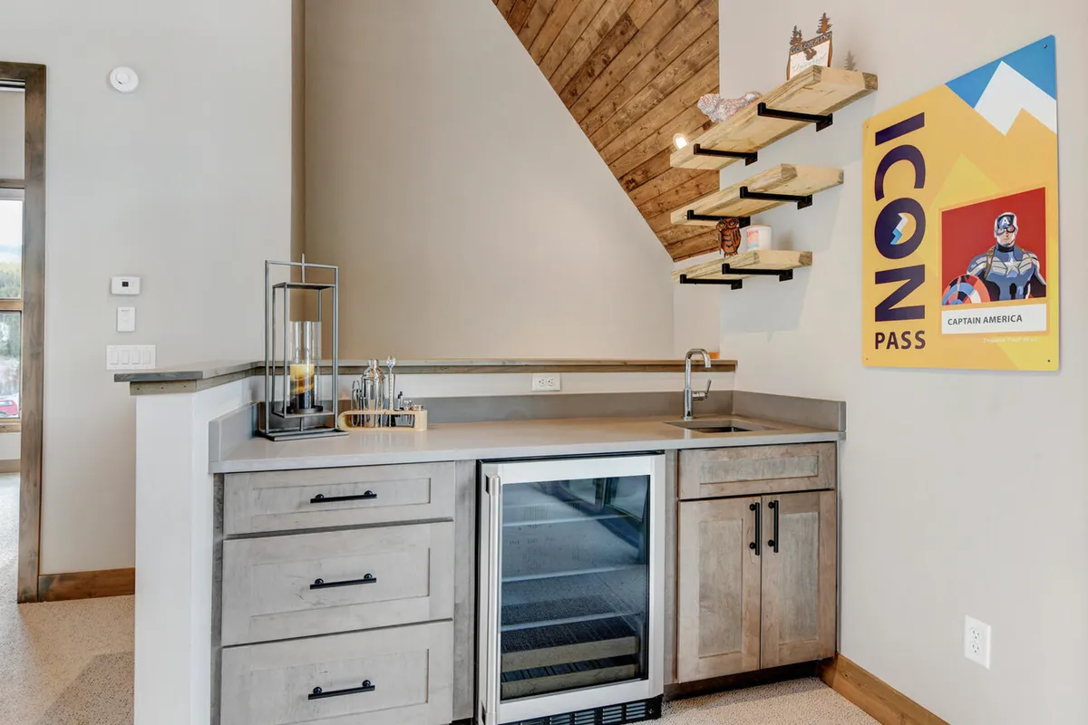 A compact yet welcoming kitchenette space with well-organized shelves and a prominent ICON Pass poster. The area is ideal for preparing drinks and snacks, supporting entertaining and socializing in a casual rec room environment.